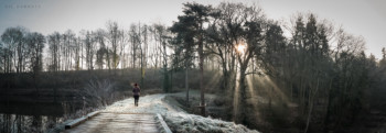 Female walker in red winter hat walks along frosty, lakeside woodland path.