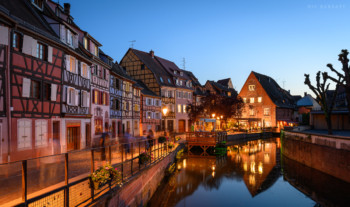 Colourful French timber buildings facing a cobble street and waterway at dusk.