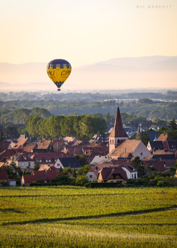 Yellow and blue hot air balloon floats above French village.