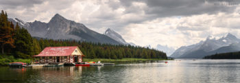 Red-roofed timber boat house on the edge of vast and mountainous Maligne Lake in the Canadian Rockies.