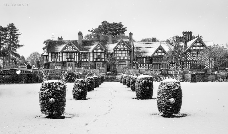 Old timber and brick country manor and surrounding gardens covered by snow.