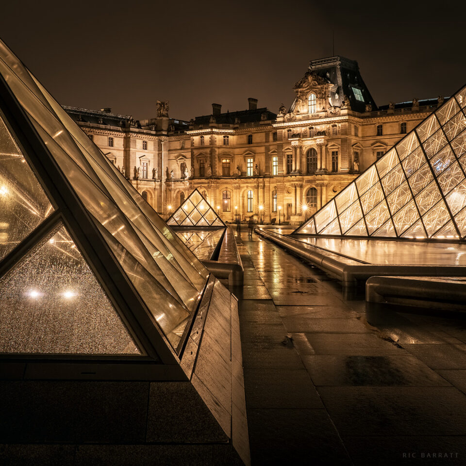 Three glass pyramids surrounded by the classic Parisian buildings of the Louvre.