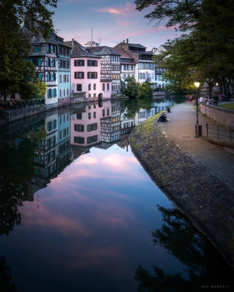 A clam, peaceful river leads its way past the half-timbered houses at dusk.
