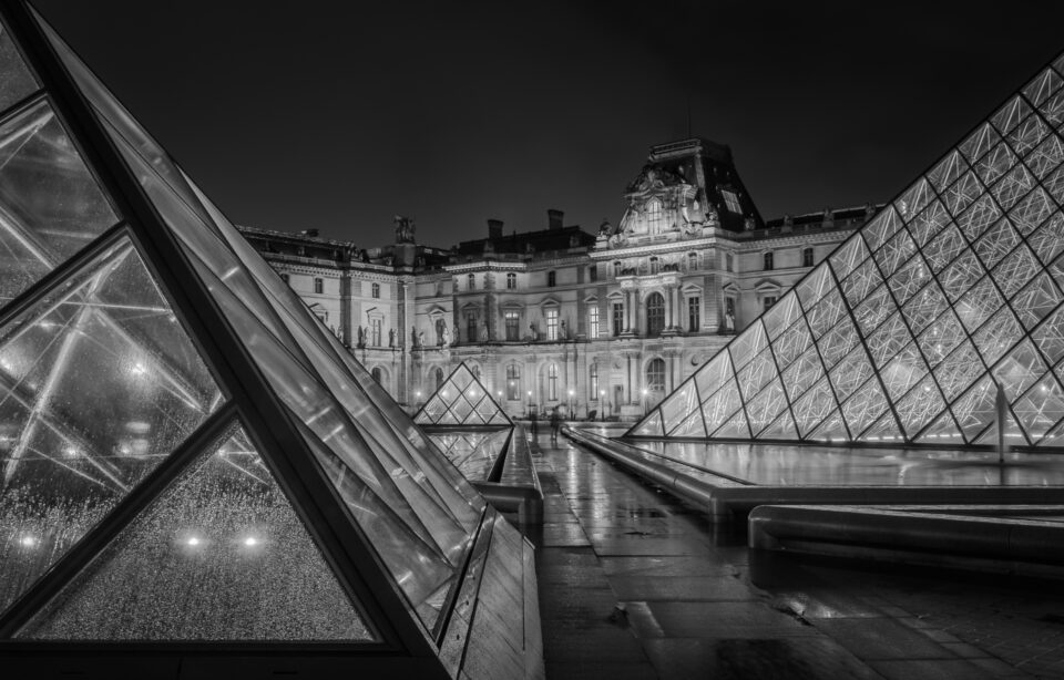 Night view of Louvre Museum with illuminated glass pyramids in black and white.