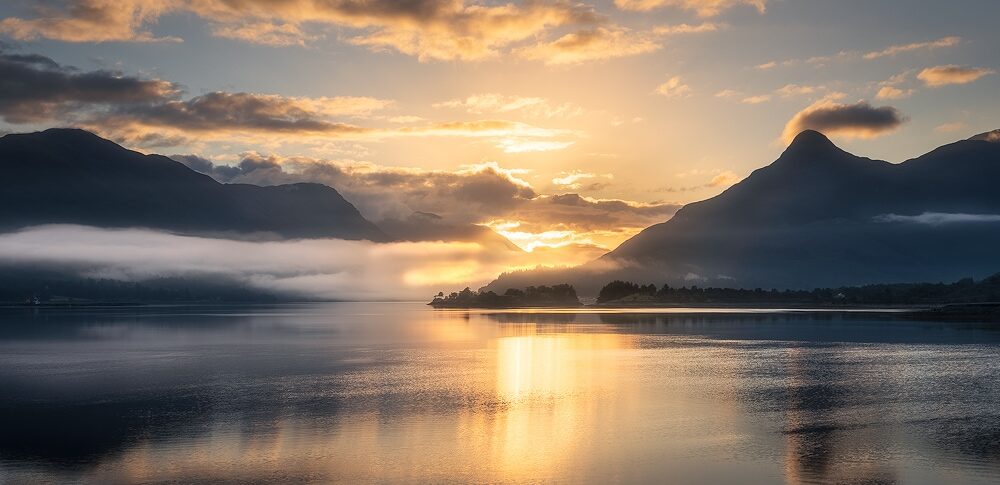 Sunrise over a lake surrounded by mountains.