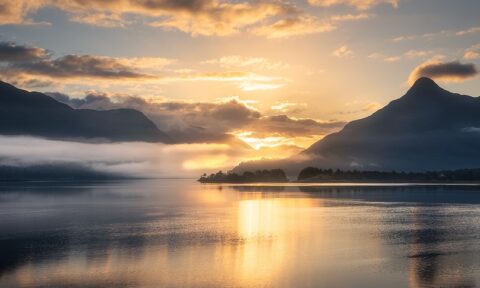 Sunrise over a lake surrounded by mountains.