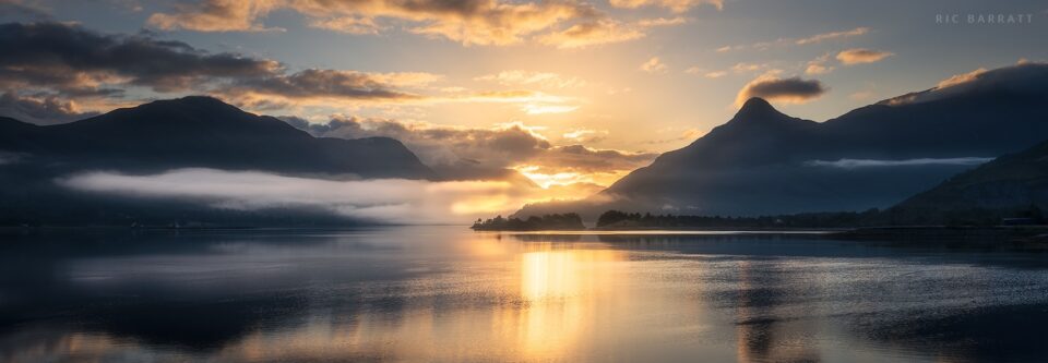 Sunrise over a lake surrounded by mountains.
