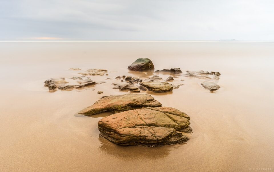 Collection of rocks on a wide empty beach.