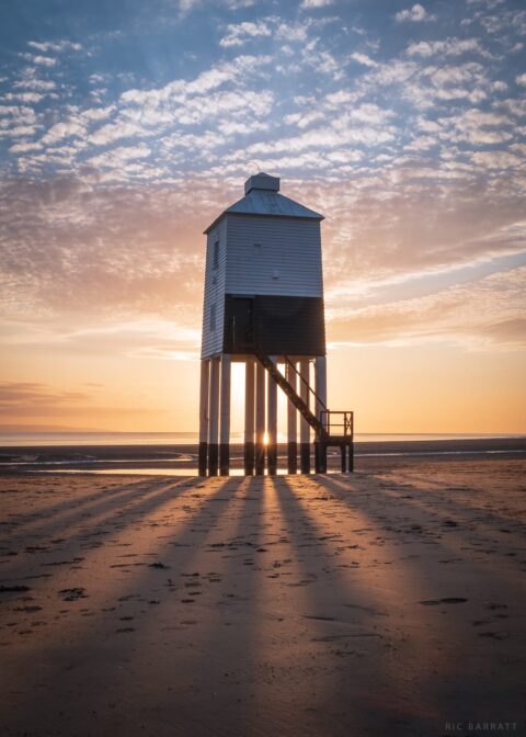 Lighthouse on stilts surrounded by sandy beach.