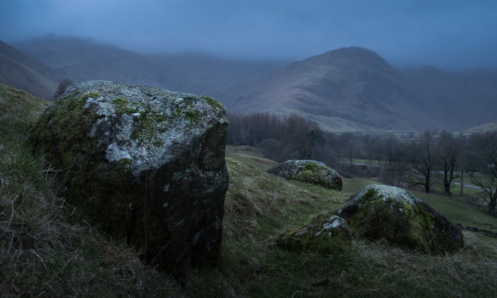 Mossy rocks in a field surrounded by mountains and trees.