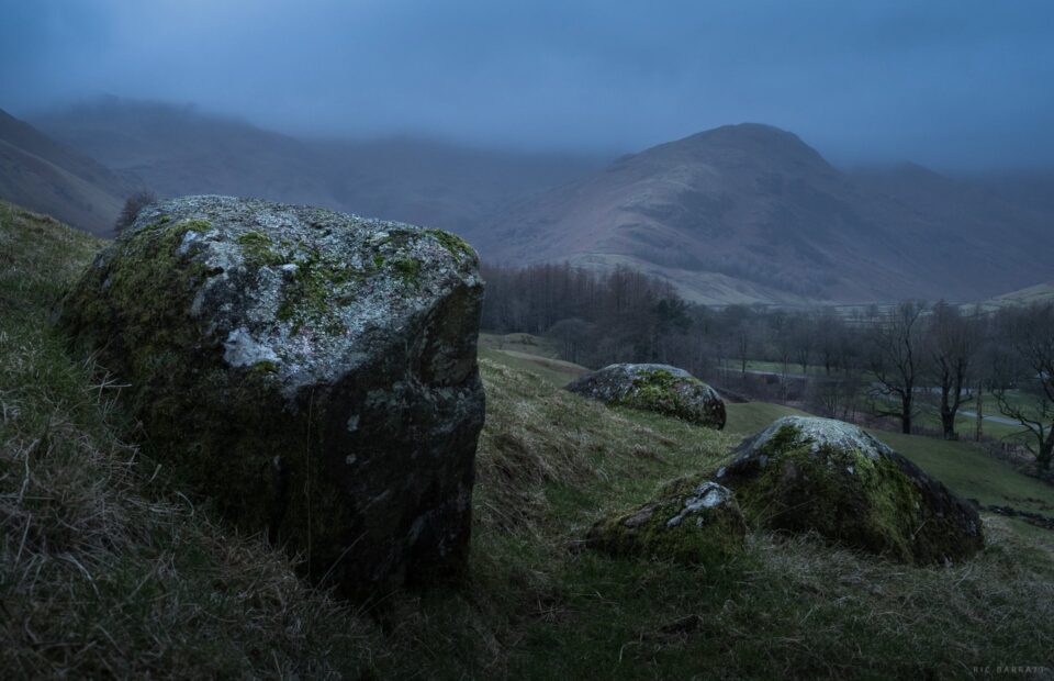 Mossy rocks in a field surrounded by mountains and trees.