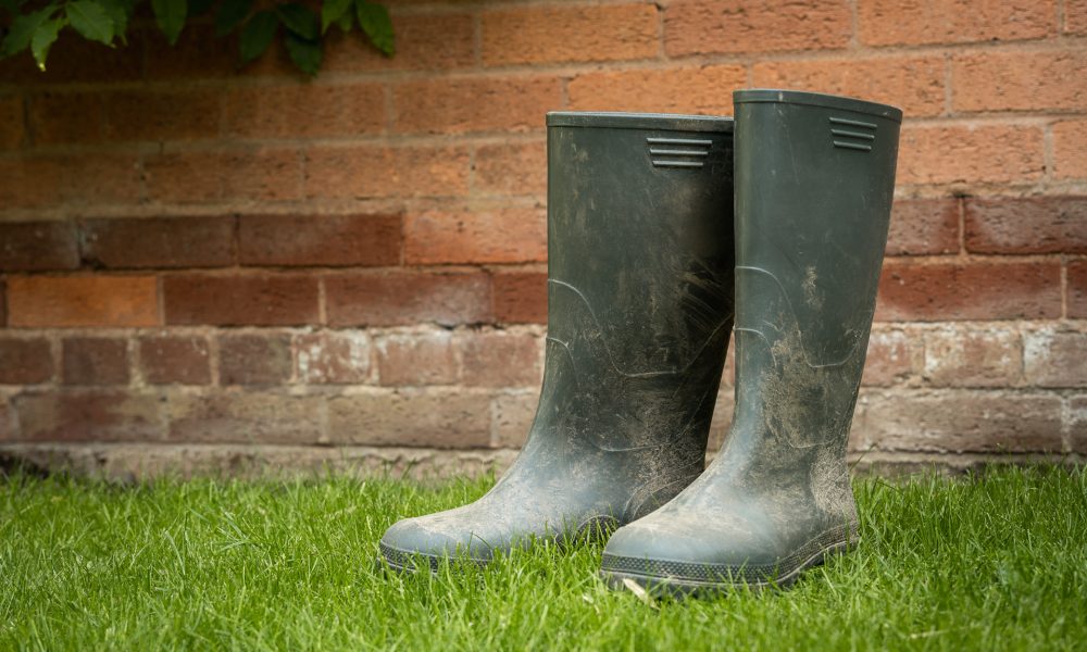 A pair of dirty green wellies next to a brick wall.
