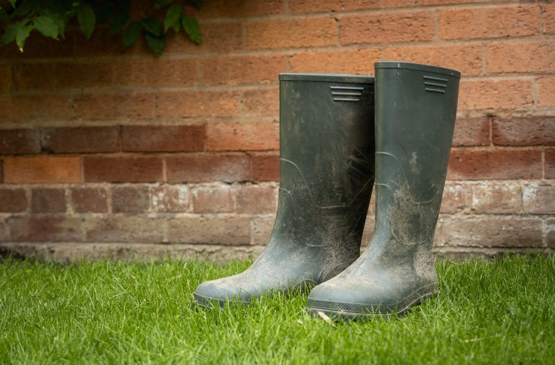 A pair of dirty green wellies next to a brick wall.