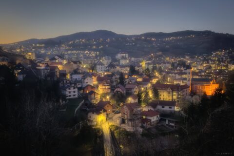 Twilight view of Jajce town with illuminated buildings and mountains in the background.