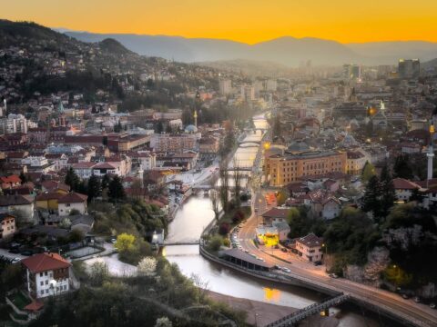 Sunset over Sarajevo with vibrant orange sky and cityscape illuminated at dusk.