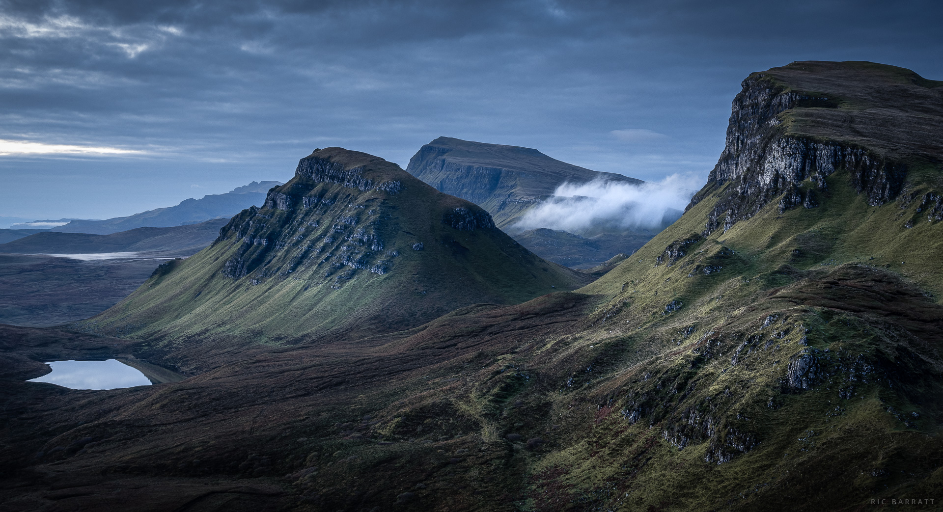 Majestic mountain landscape with rolling green hills and misty peaks under a cloudy sky.