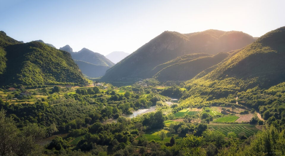 A lush green valley surrounded by towering mountains at sunrise.