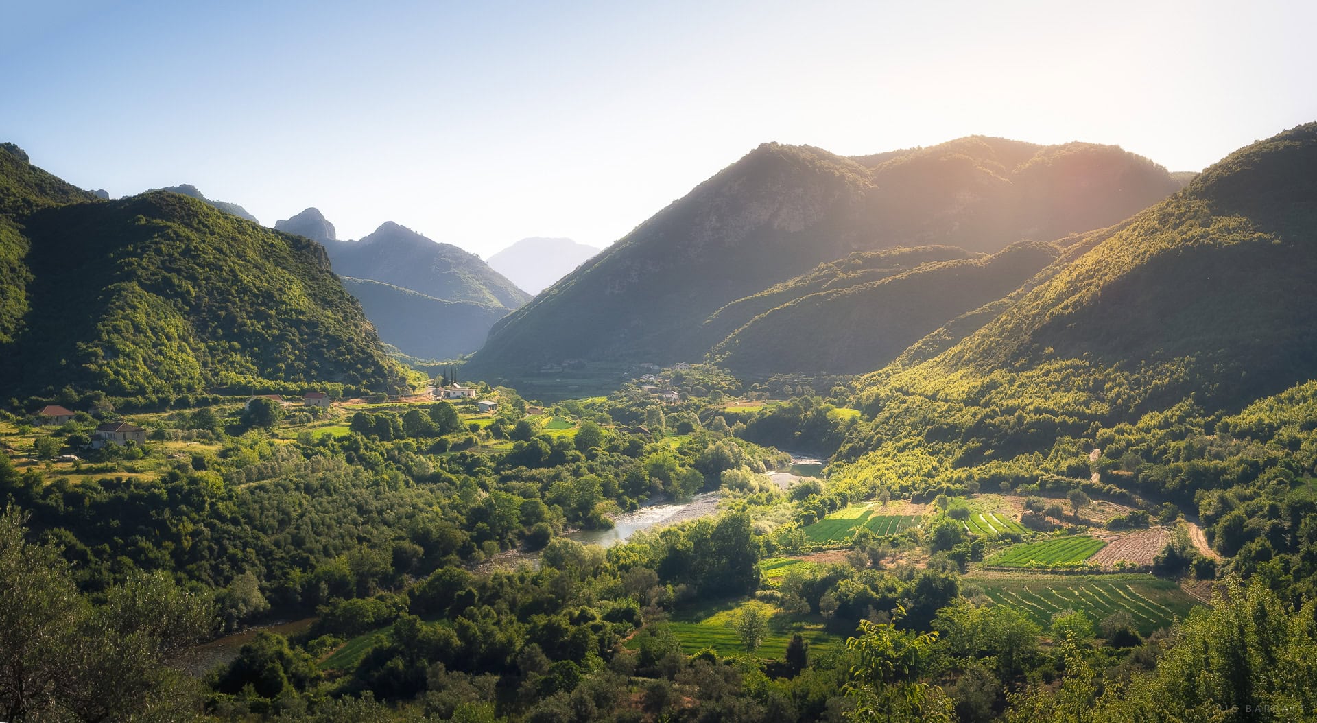 A lush green valley surrounded by towering mountains at sunrise.