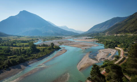Mountain river flowing through lush green valley with towering mountains in the background.