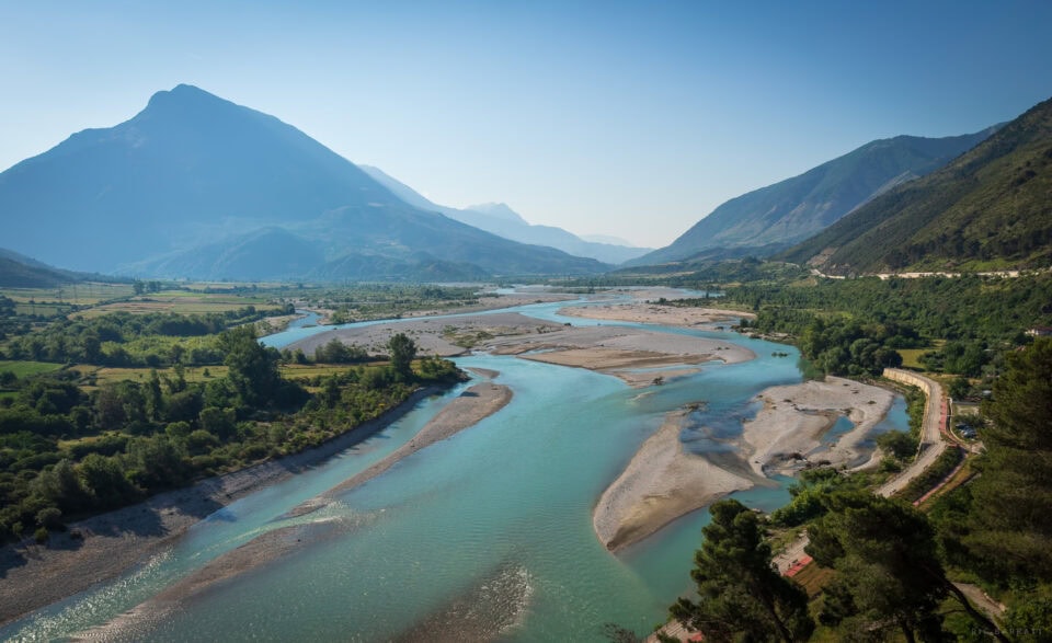 Mountain river flowing through lush green valley with towering mountains in the background.