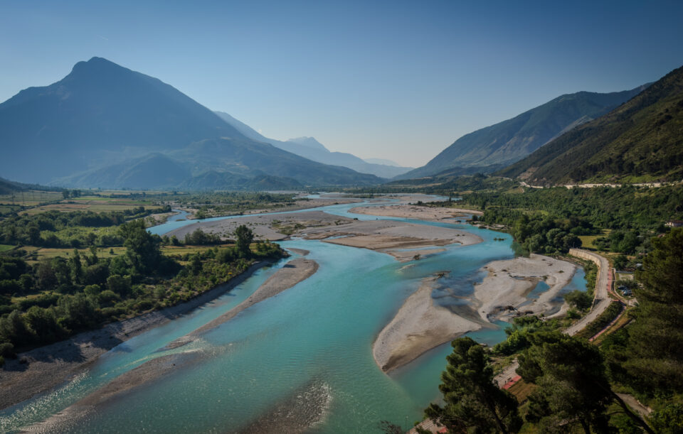 Mountain river flowing through lush green valley with towering mountains in the background.