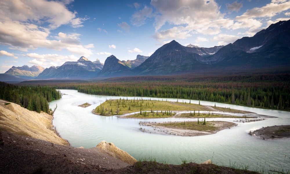 Vivid landscape of winding river and majestic mountains under a partly cloudy sky.