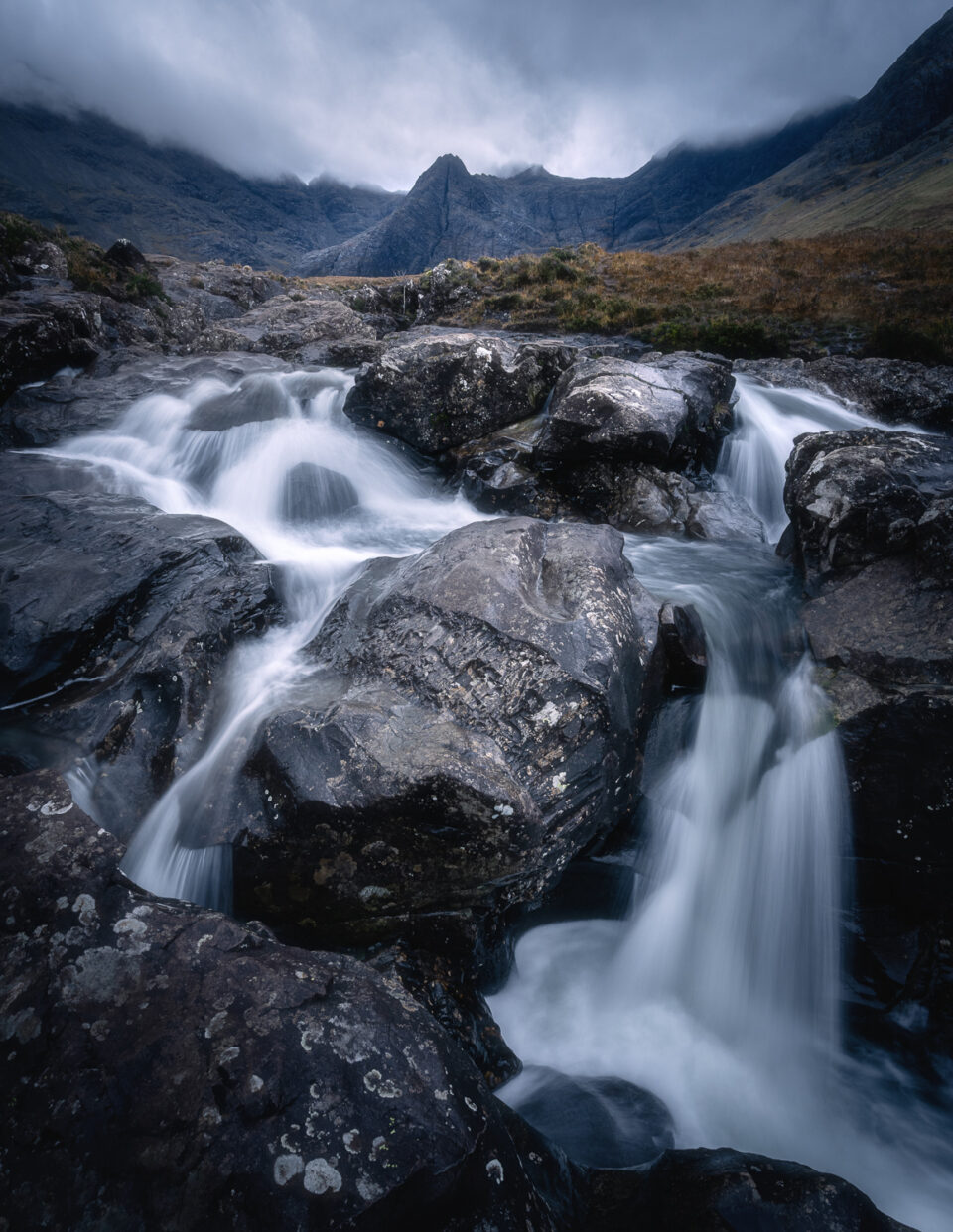Scenic waterfall in the Scottish Highlands with rugged mountains in the background.