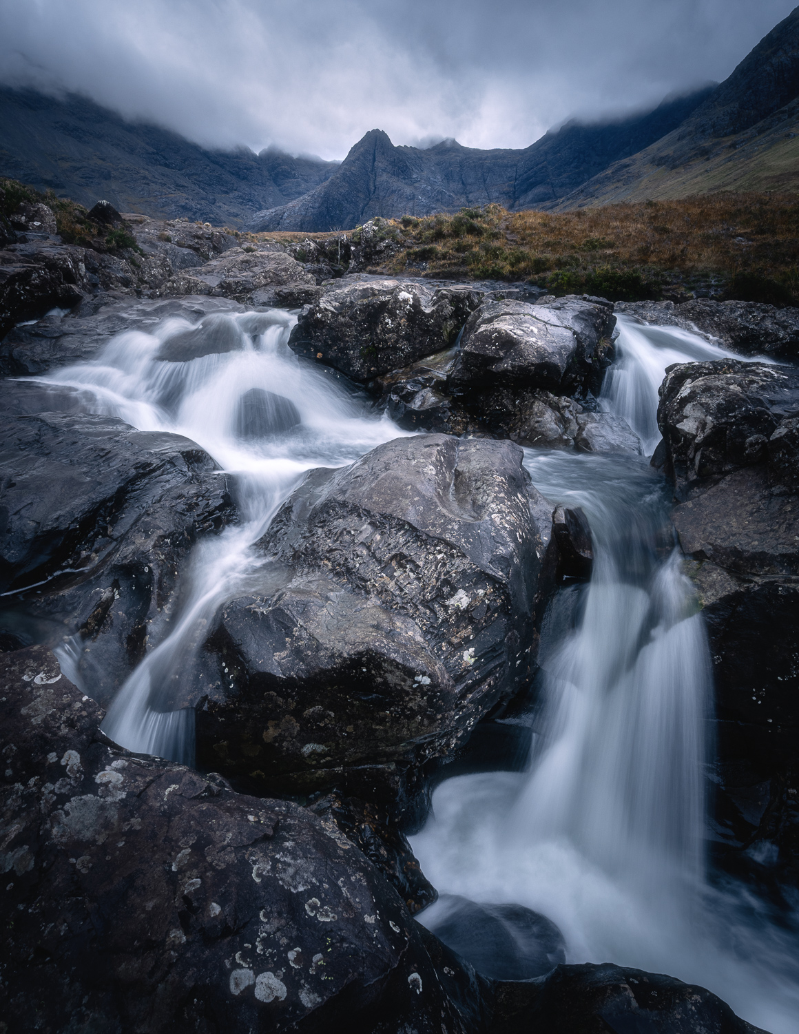 Scenic waterfall in the Scottish Highlands with rugged mountains in the background.