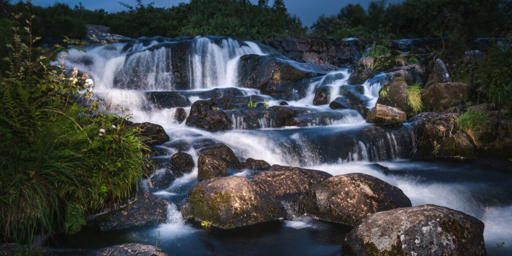 Serene waterfall cascading over rocks in a lush green landscape at dusk.