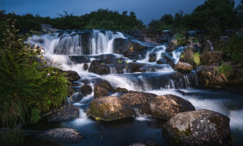 Serene waterfall cascading over rocks in a lush green landscape at dusk.