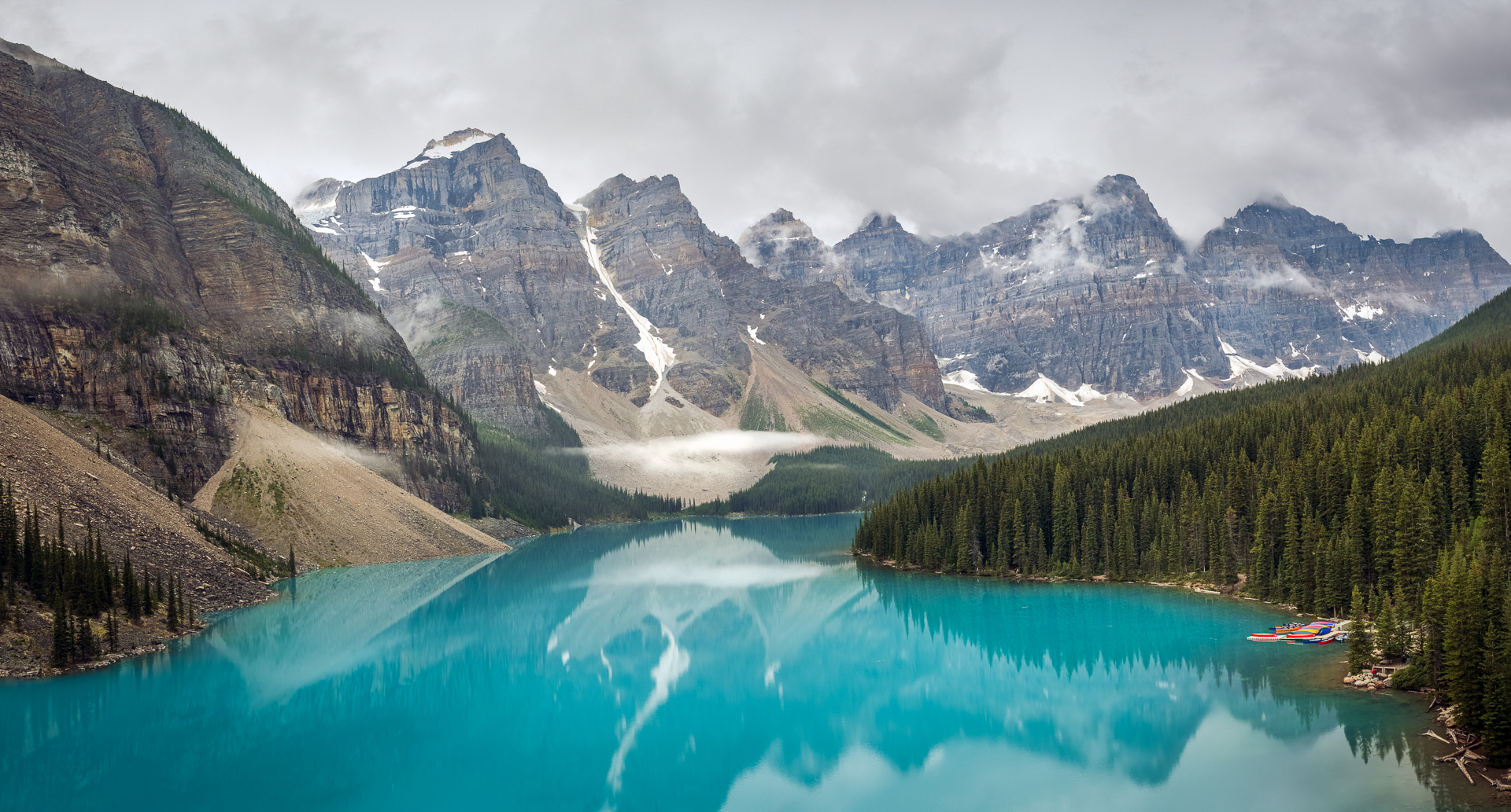 Moraine Lake surrounded by towering mountain peaks and lush green forests.
