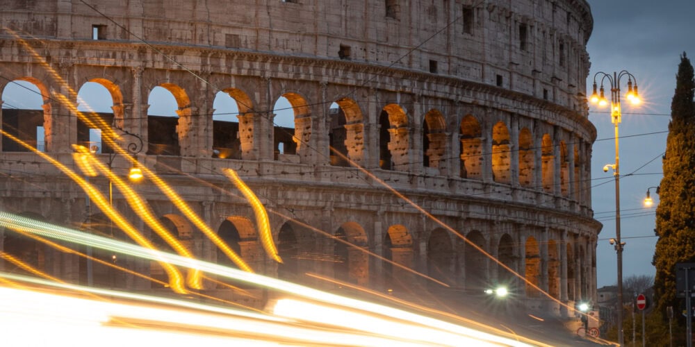 Long exposure of traffic passing near the Colosseum in Rome at dusk.