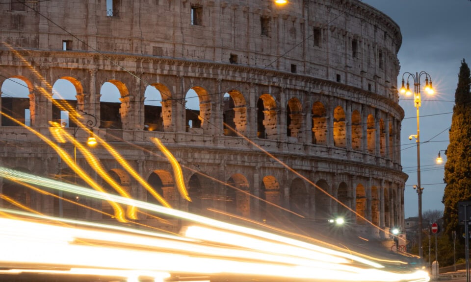 Long exposure of traffic passing near the Colosseum in Rome at dusk.