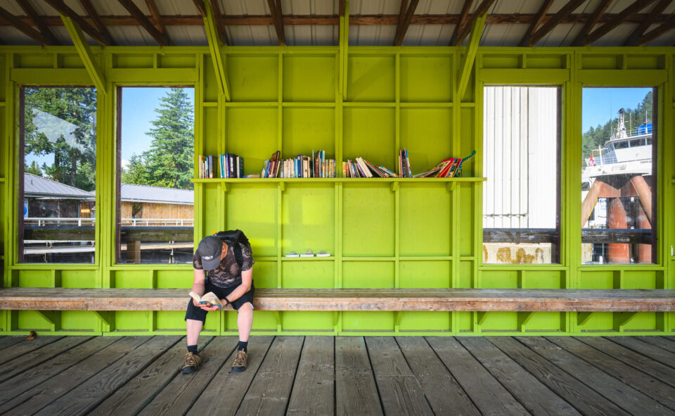 Person sitting on a bench reading a book inside a vibrant green structure.