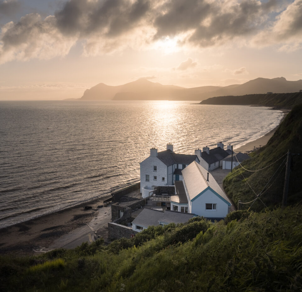 Scenic view of Porth Dinllaen coast at sunrise with white cottages and rolling hills.
