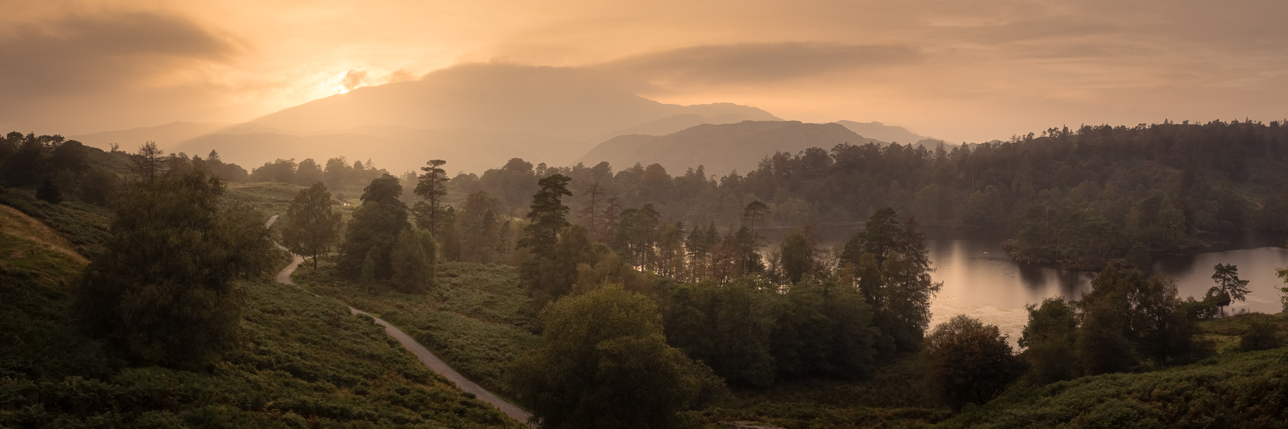 Stormy sky over Tarn Hows with dark clouds and a setting sun.