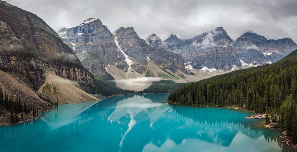Mountain landscape with evergreen forest, cloudy skies and vivid turquoise lake.